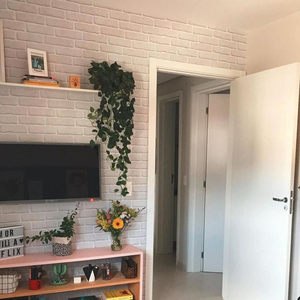 Papel De Parede Adesivo Autocolante Tijolo Rústico Branco aplicado atrás da televisão, junto com algumas plantas.